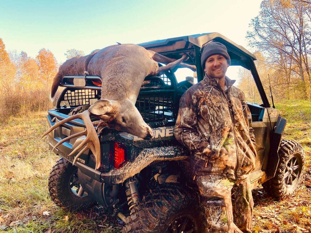 A hunter stands beside a Polaris General UTV with a dropped whitetail deer on the tailgate.