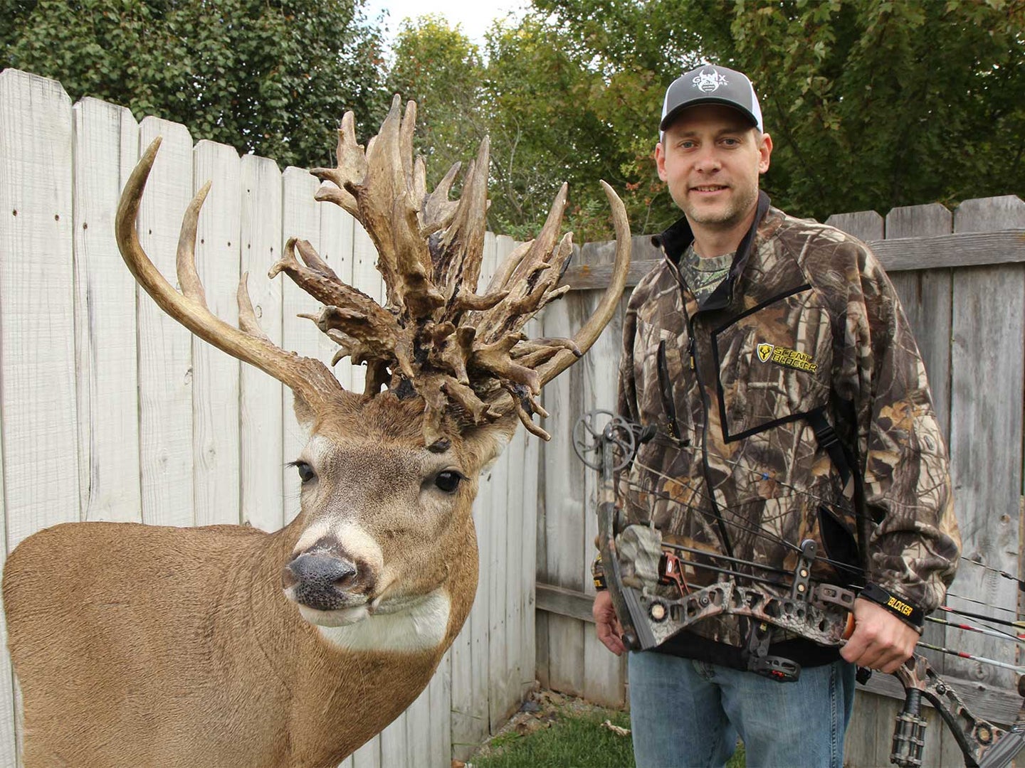 A hunter standing next to a large whitetail buck with a nontypical antler spread.