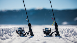 Clam ice fishing lures and reels sitting on frozen lake