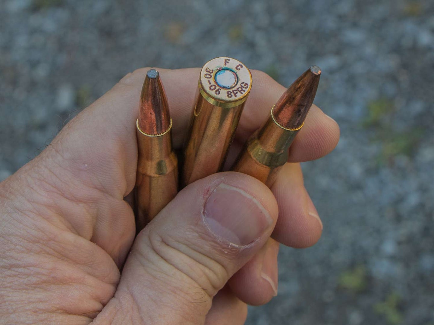A hand holds three rifle bullets.