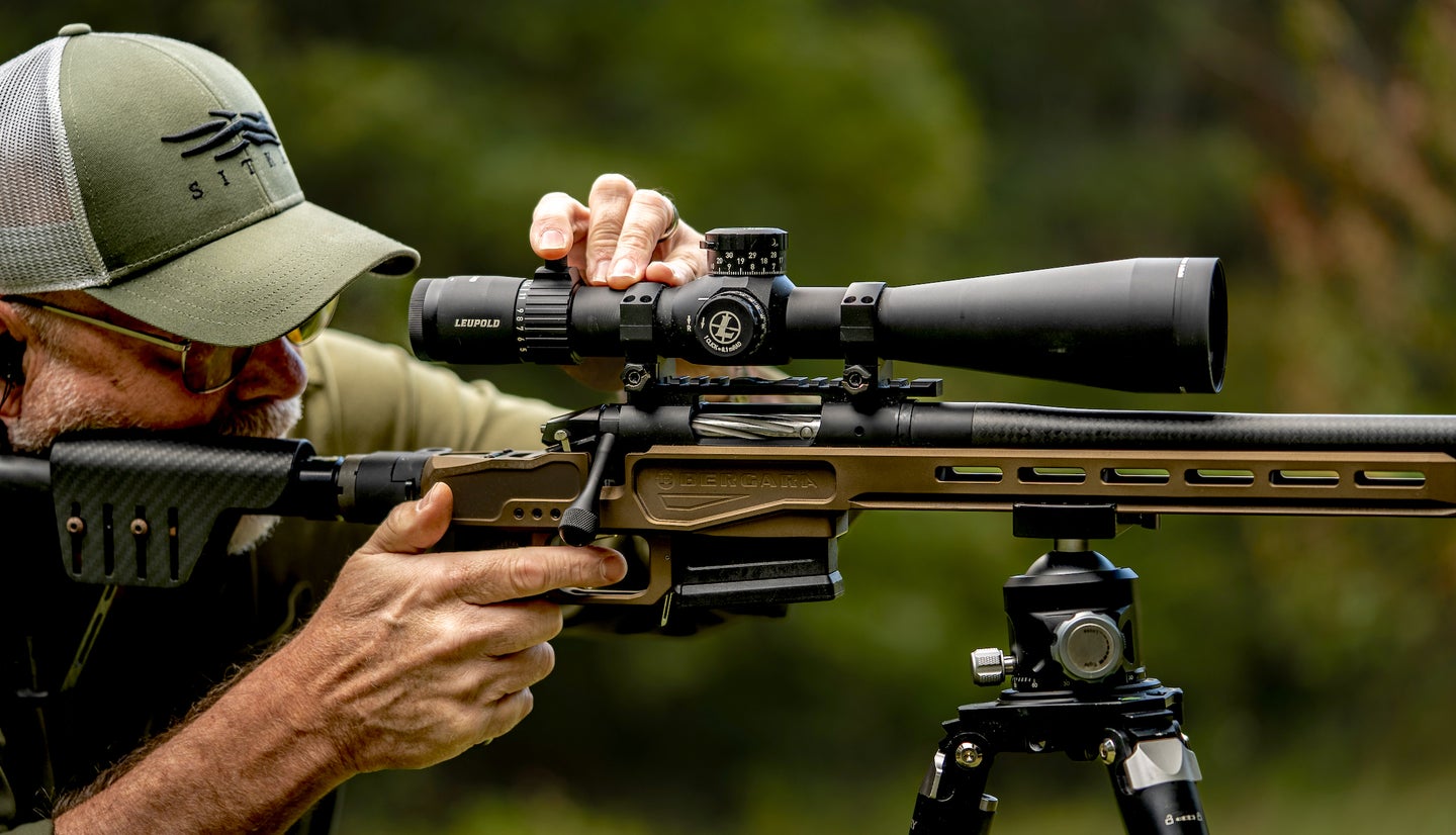 Man shooting a scoped rifle on a tripod.