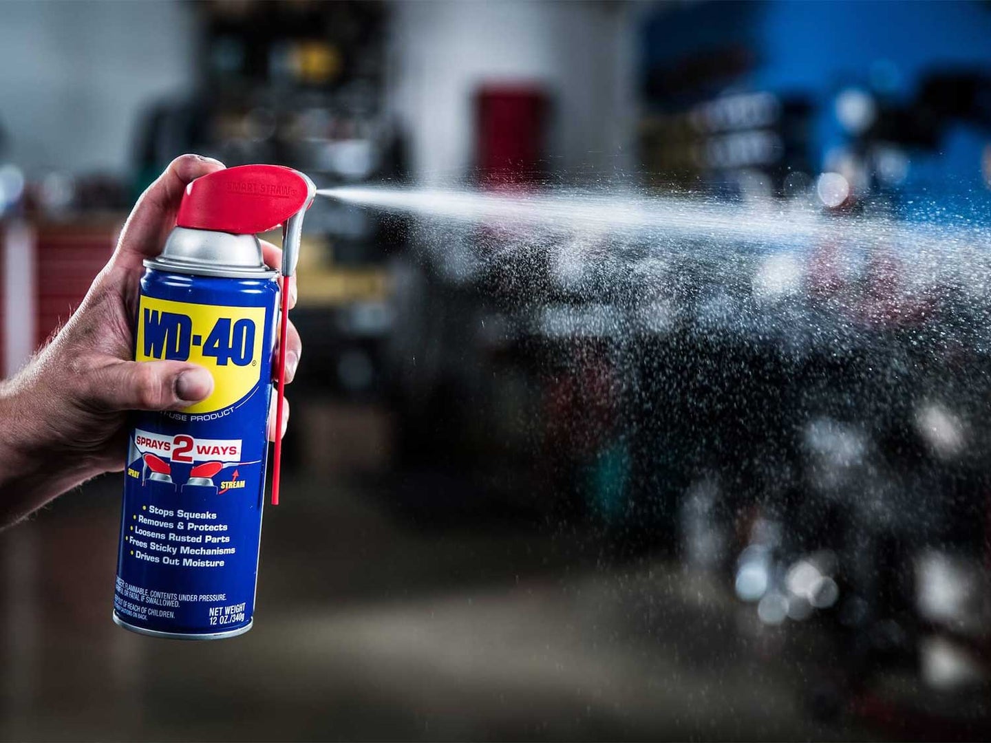 A person spraying a can of WD40 in a garage.