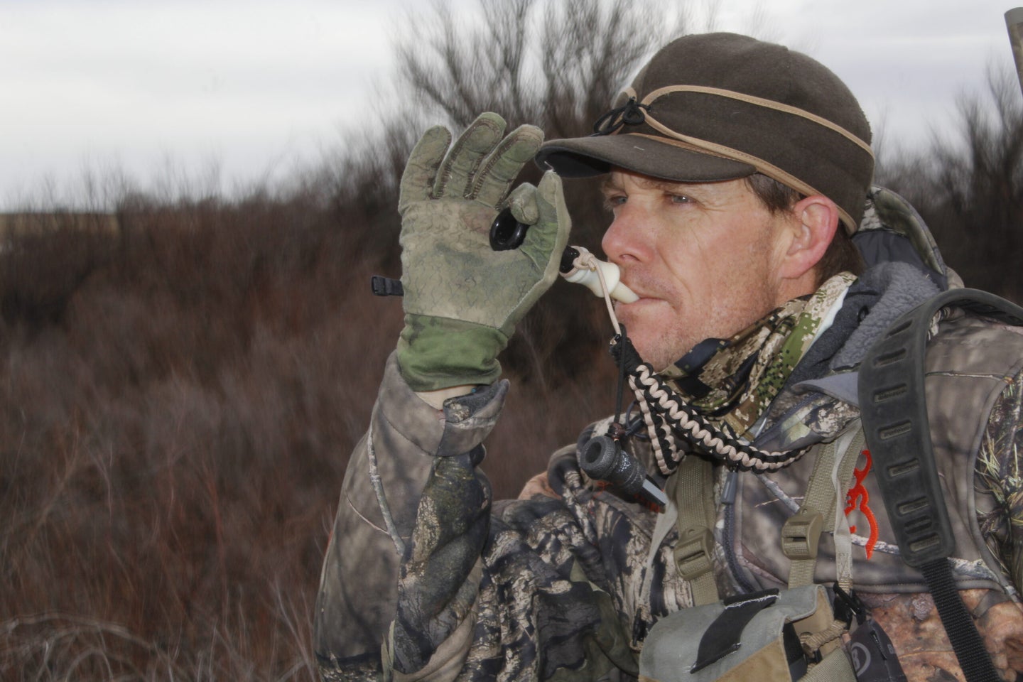 Hunter wearing camouflage blowing on a coyote call.