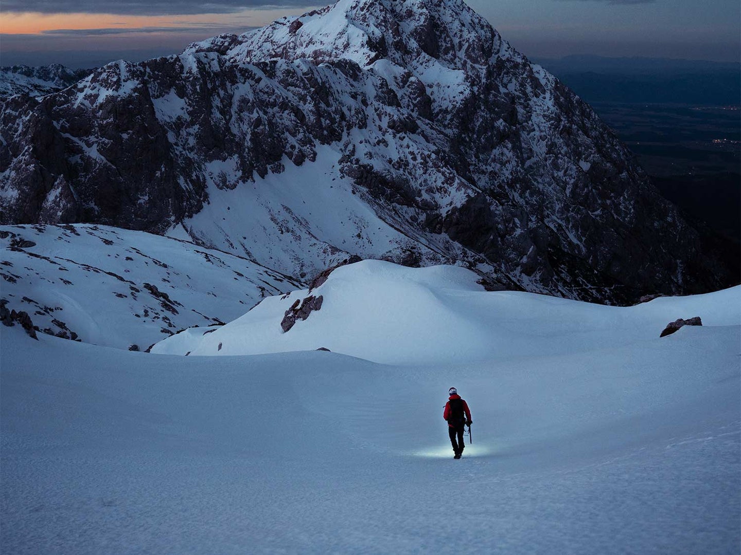 A person walks through the snow on the mountain side.