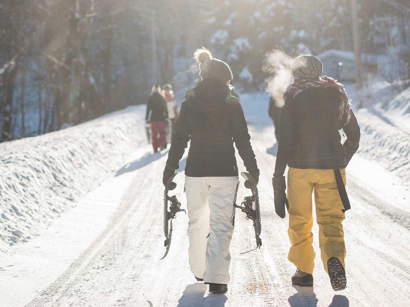Man and woman hiking while carrying snowshoes and wearing long underwear to stay warm.
