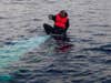 A man sits stranded on a capsized boat at sea.