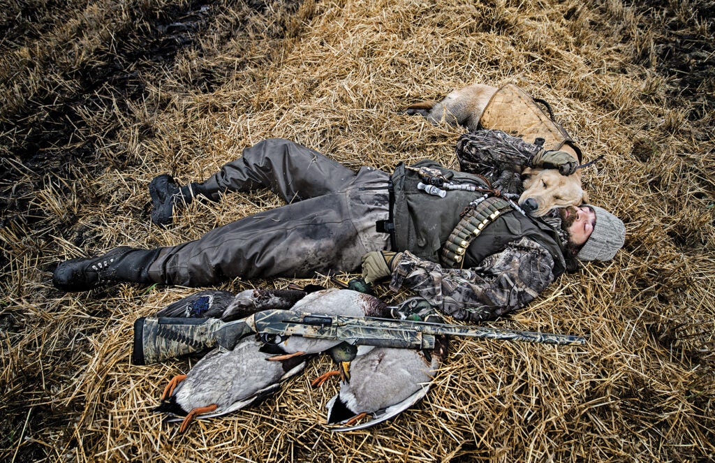 Hunter lying on the ground with his hunting dog.