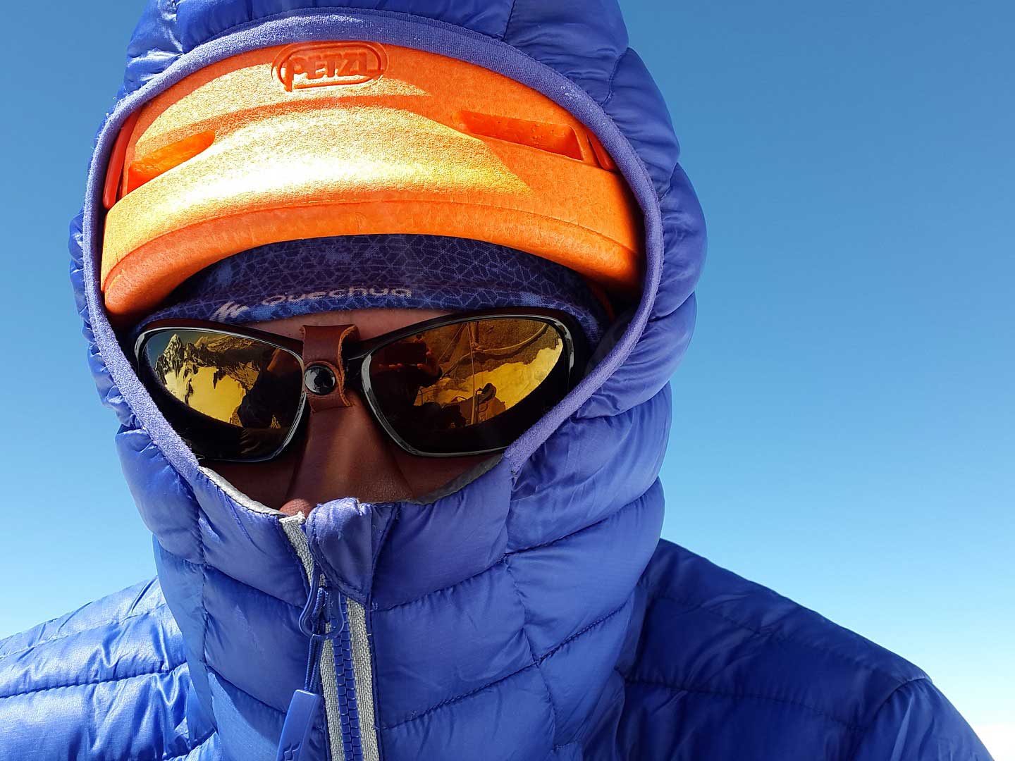 Person wearing a blue parka, orange hat, and glacier glasses.