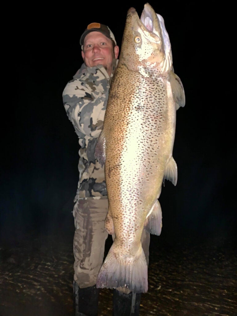 A man holds up a gigantic brown trout.