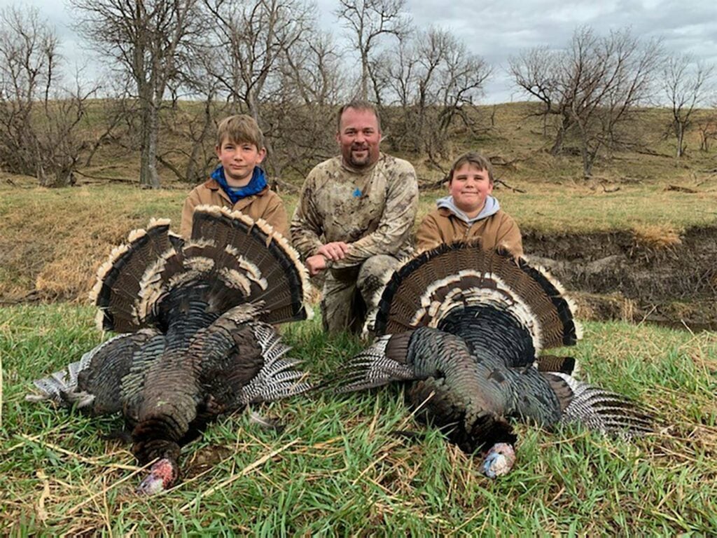 A hunter and two kids stands behind two turkeys.