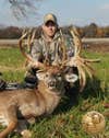 A hunter kneels beside a large whitetail buck.
