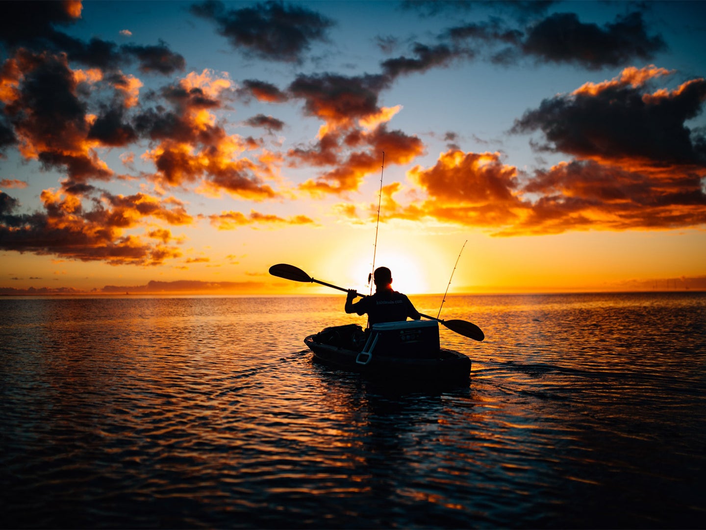A single person in a canoe paddles across a lake with the sun setting in the background.
