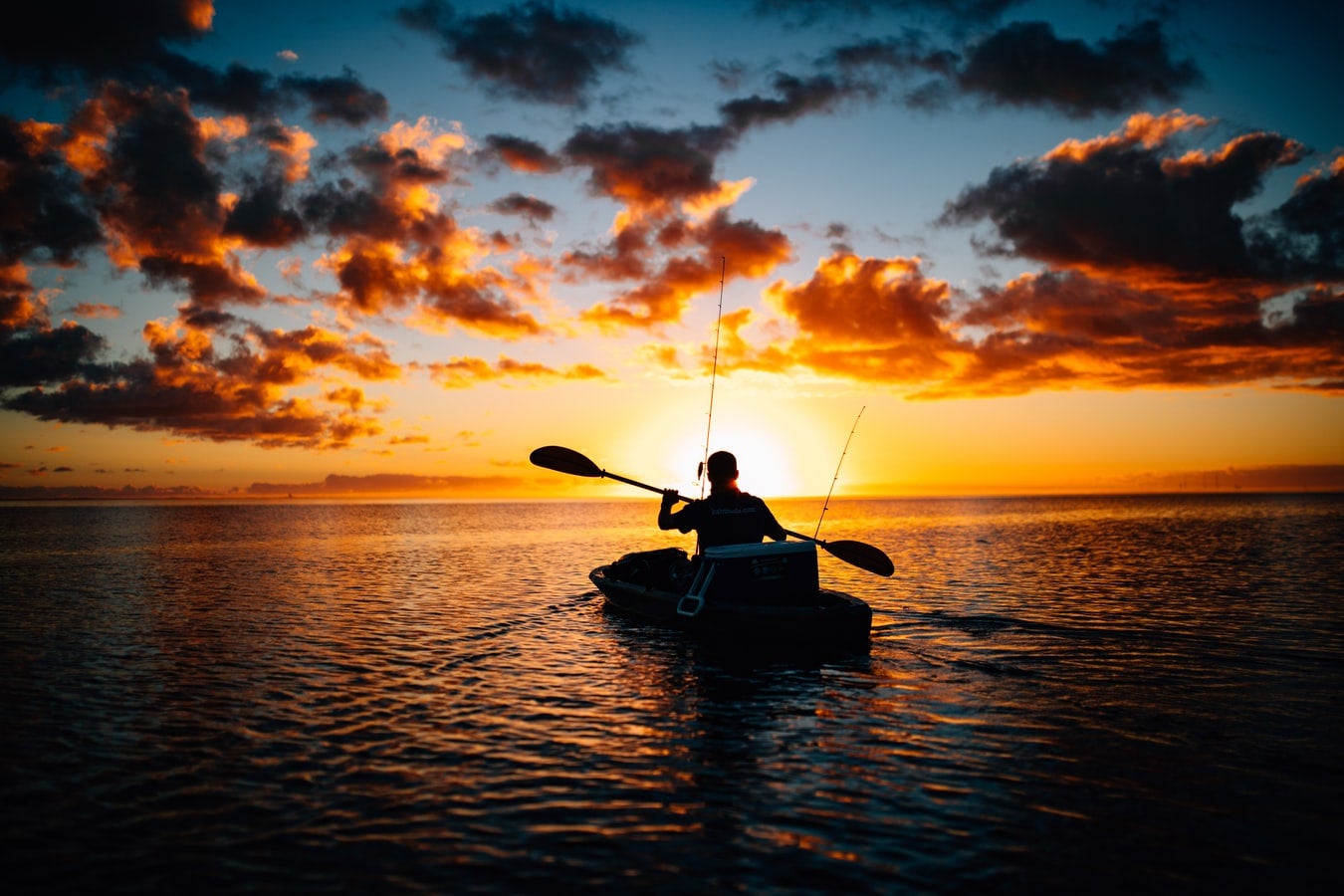 An angler paddles a kayak at dawn on a lake.