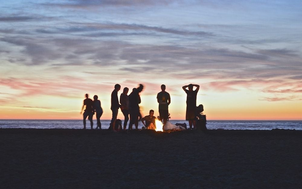 A group of people standing around a fire in the setting sun.
