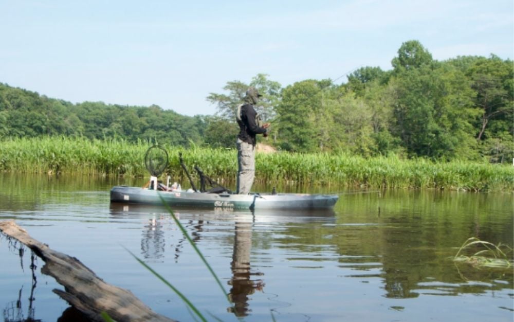 Man standing over the kayak and fishing to a lake.