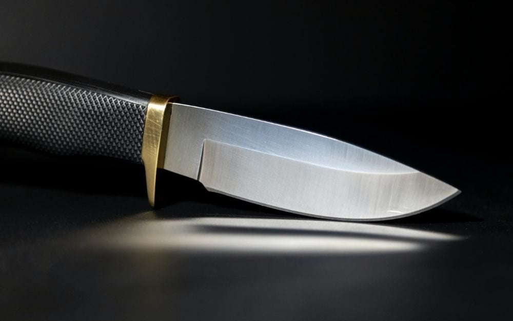 A sharpen knife standing on his curved tip with a black bottom and a gold line into it.