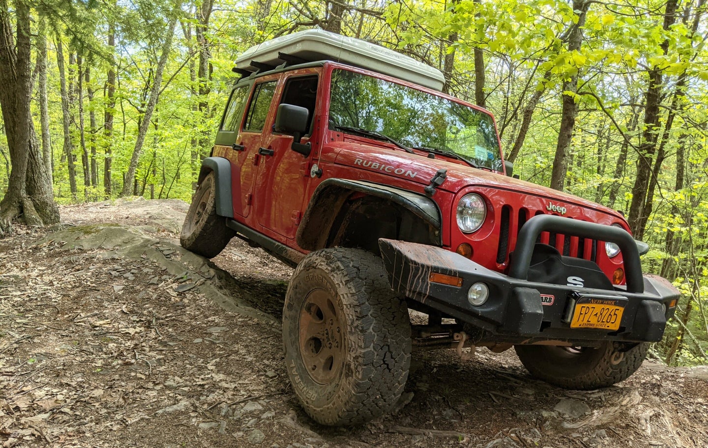 An overland jeep driving through the woods.