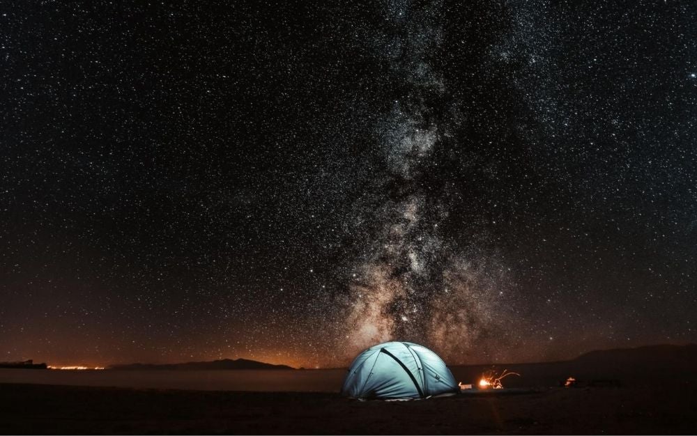 Camping tent next to a fire under the sky full of stars
