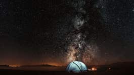 Camping tent next to a fire under the sky full of stars