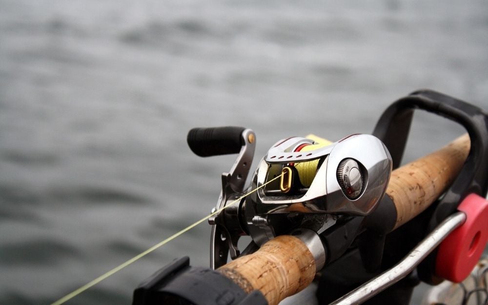 A fish hook and a silver spinning reel photographed up close in the middle of a water space.