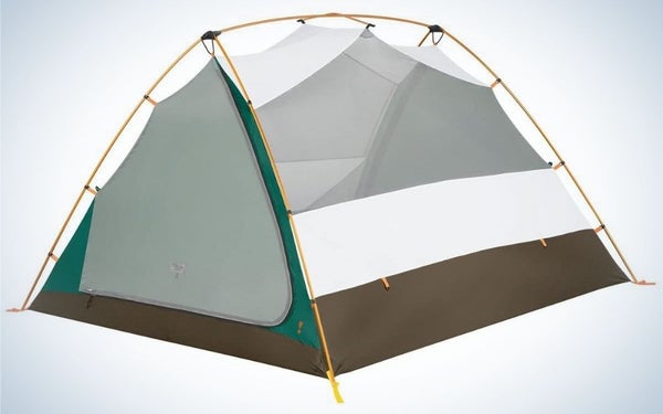 A small tent with a space at the top, which is tied and shaped like a roof at the top, white in color and with a thick brown and green stripe at the bottom and is secured with orange rope from one corner of the tent to the other .