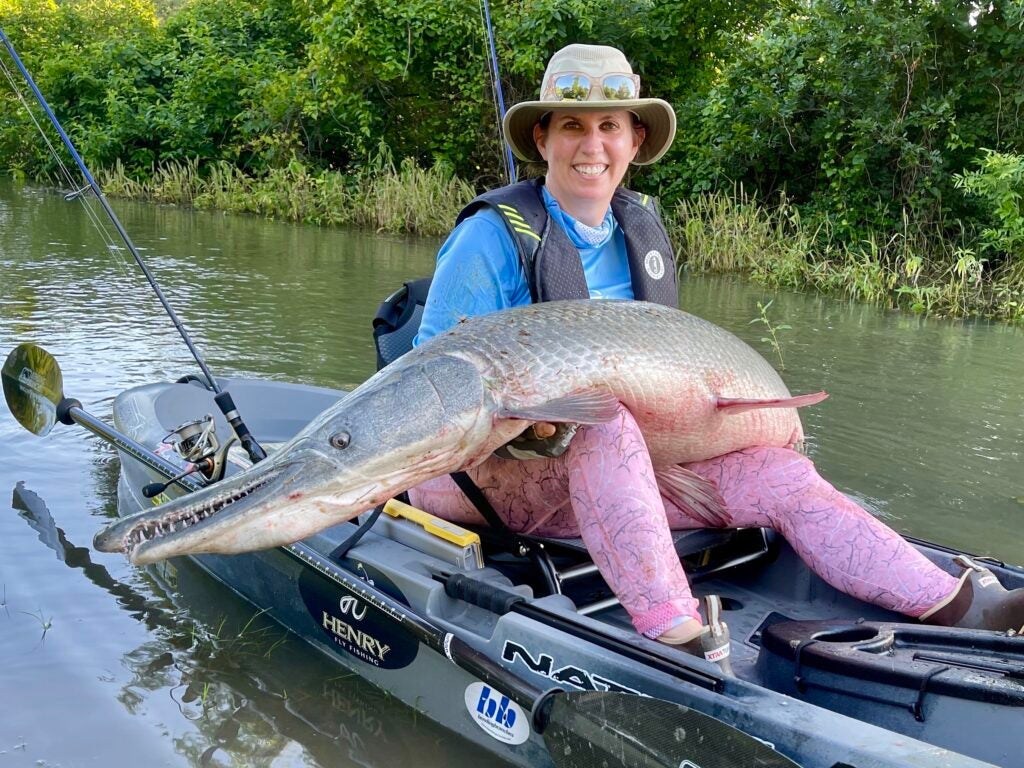 Woman holds alligator gar on kayak