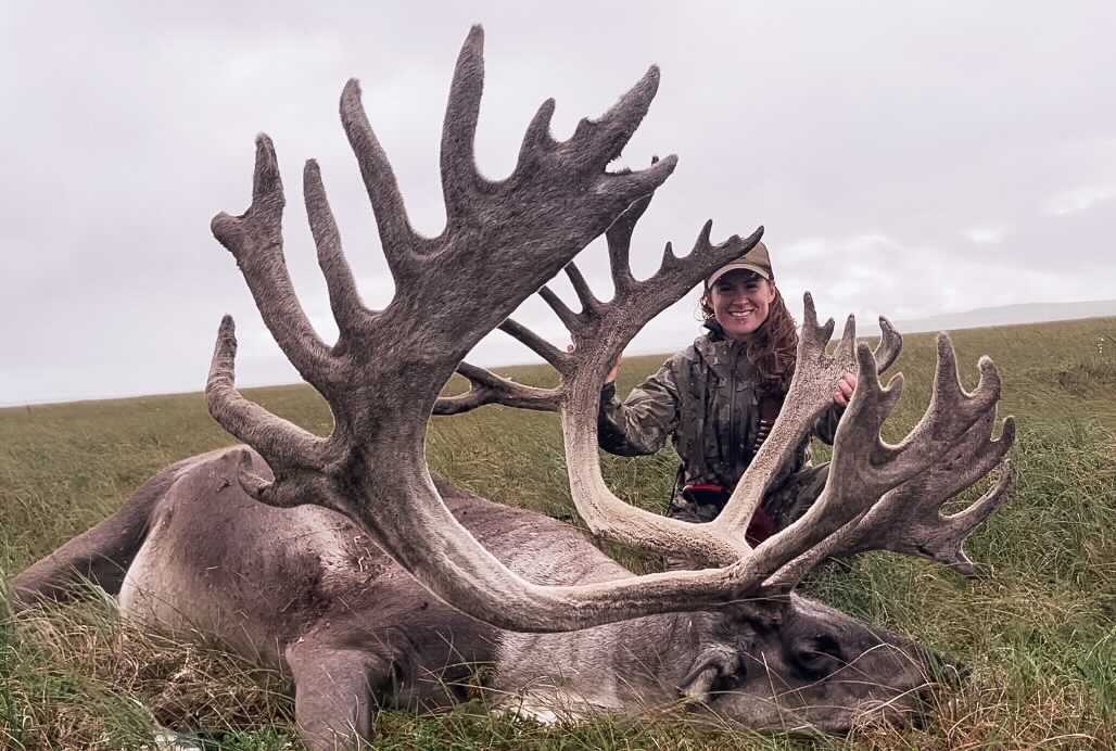 A woman stands behind the massive antlers of a dead caribou