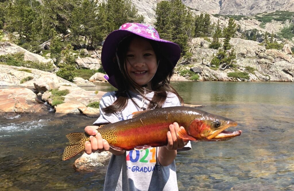 Girl holding record golden trout next to a lake.