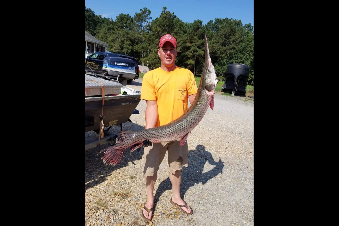 Man in yellow shirt and red t-shirt holds large gar during the day