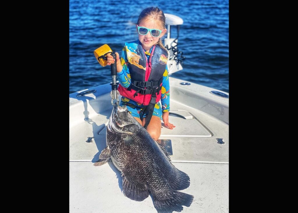 A small girl in life vests on boat with big black fish