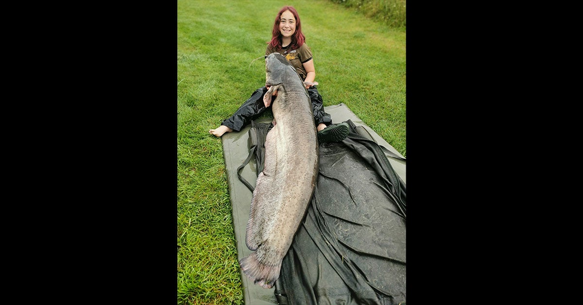 a young girl with red hair sits with long and large catfish