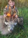 Boy wearing fluorescent orange vest poses with dead triple drop tine deer