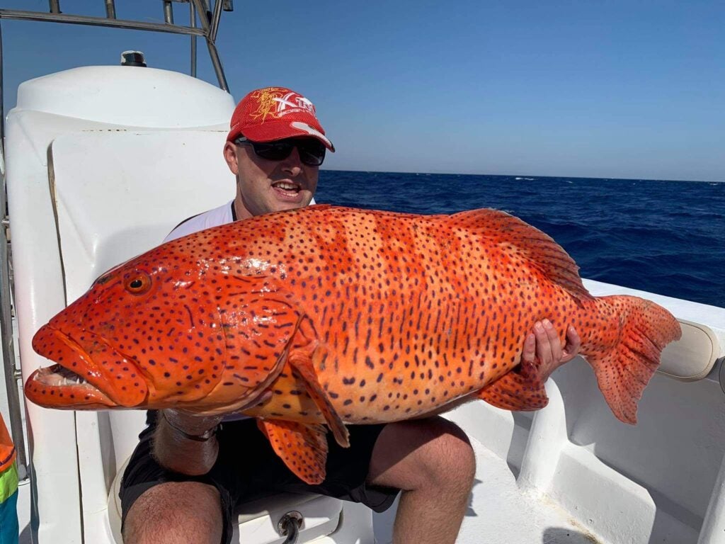 man holds large orange fish with blue speckles