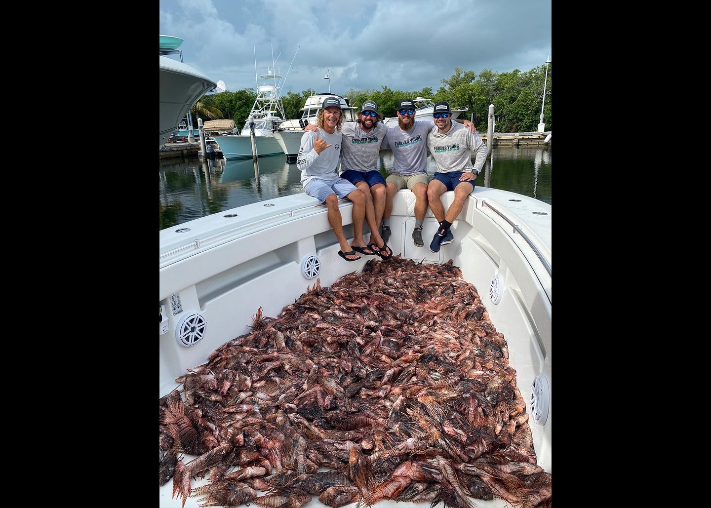 Four guys on boat with hundreds of lionfish littered across the baot