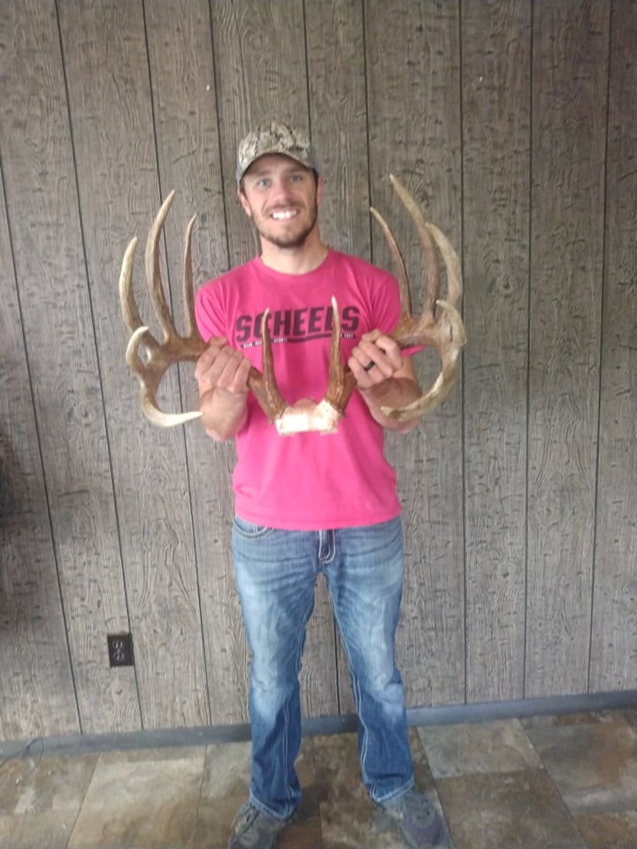 man in pink shirt holds deer large antlers