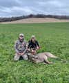 man and woman kneel next to dead buck