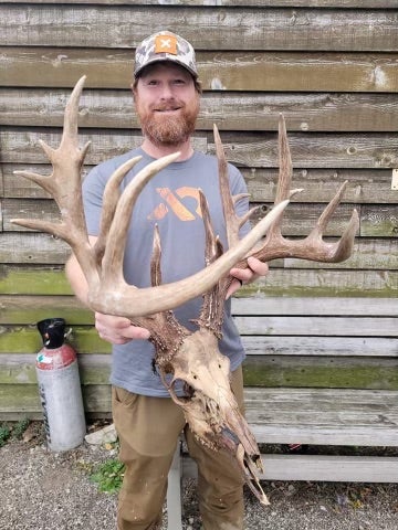 man poses with large deadhead with antlers