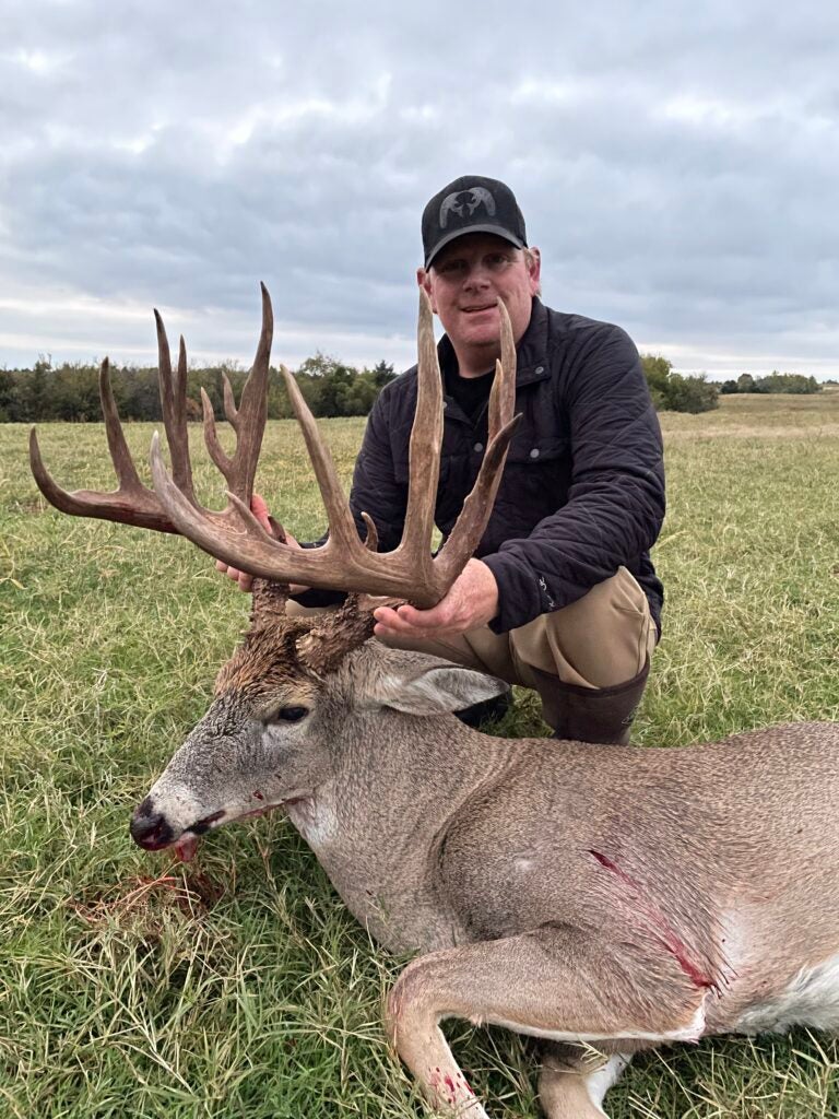 man poses with dead deer with large rack