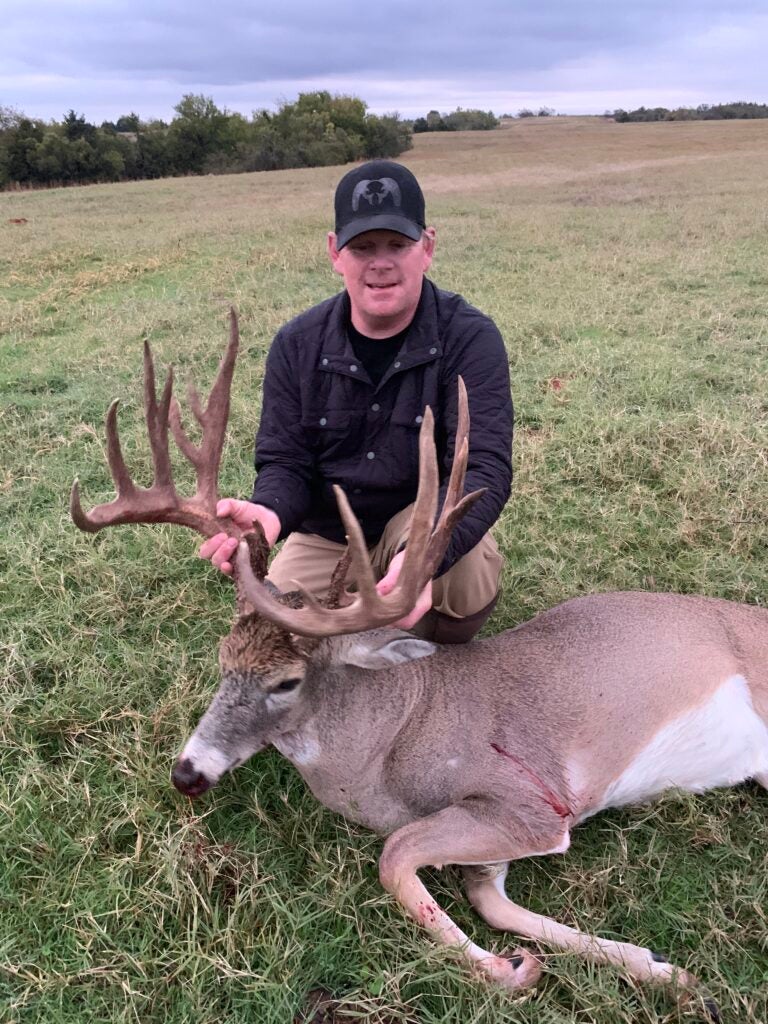man smiles with dead buck with antlers