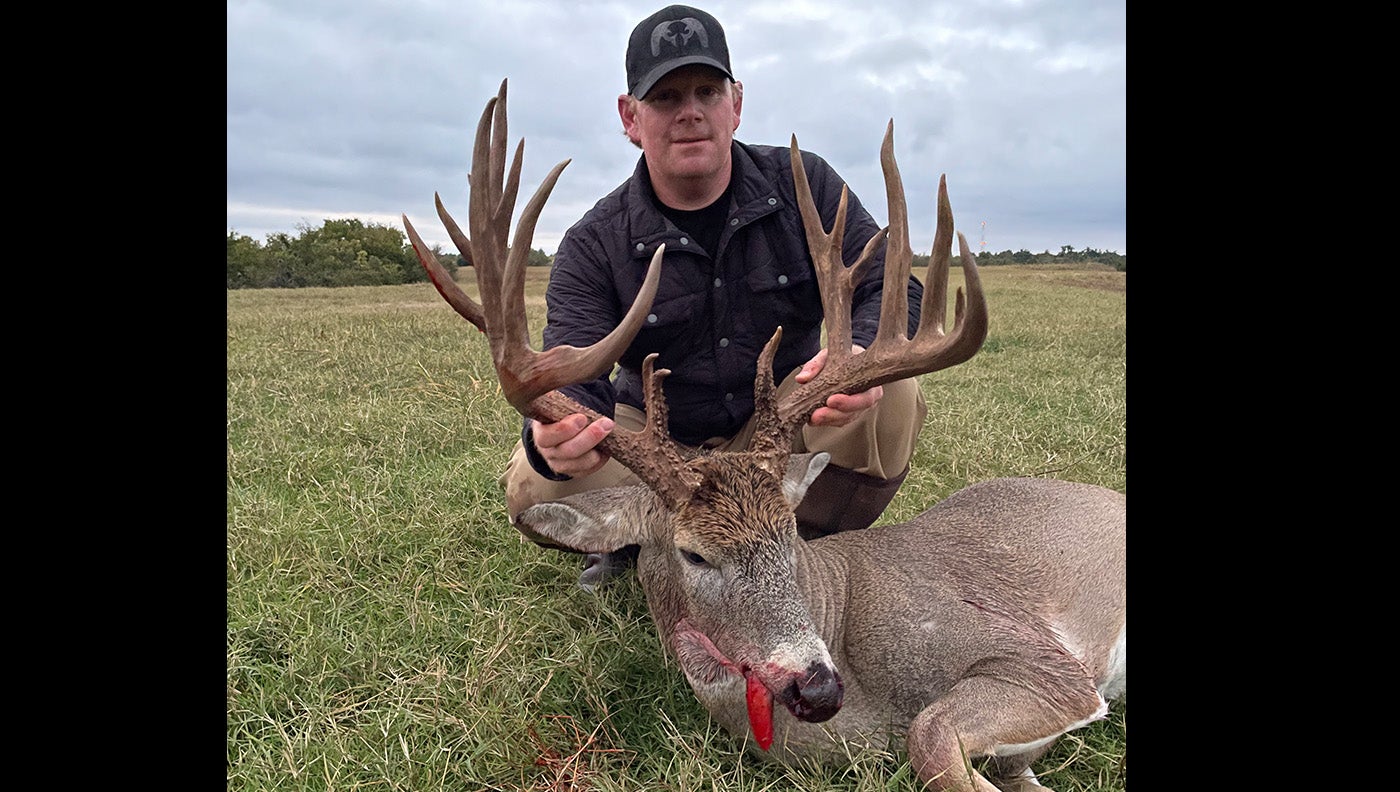 man crouches behind dead buck with large symmetrical rack of antlers