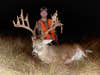 man in orange vest stands behind dead deer with incredibly large non-typical rack
