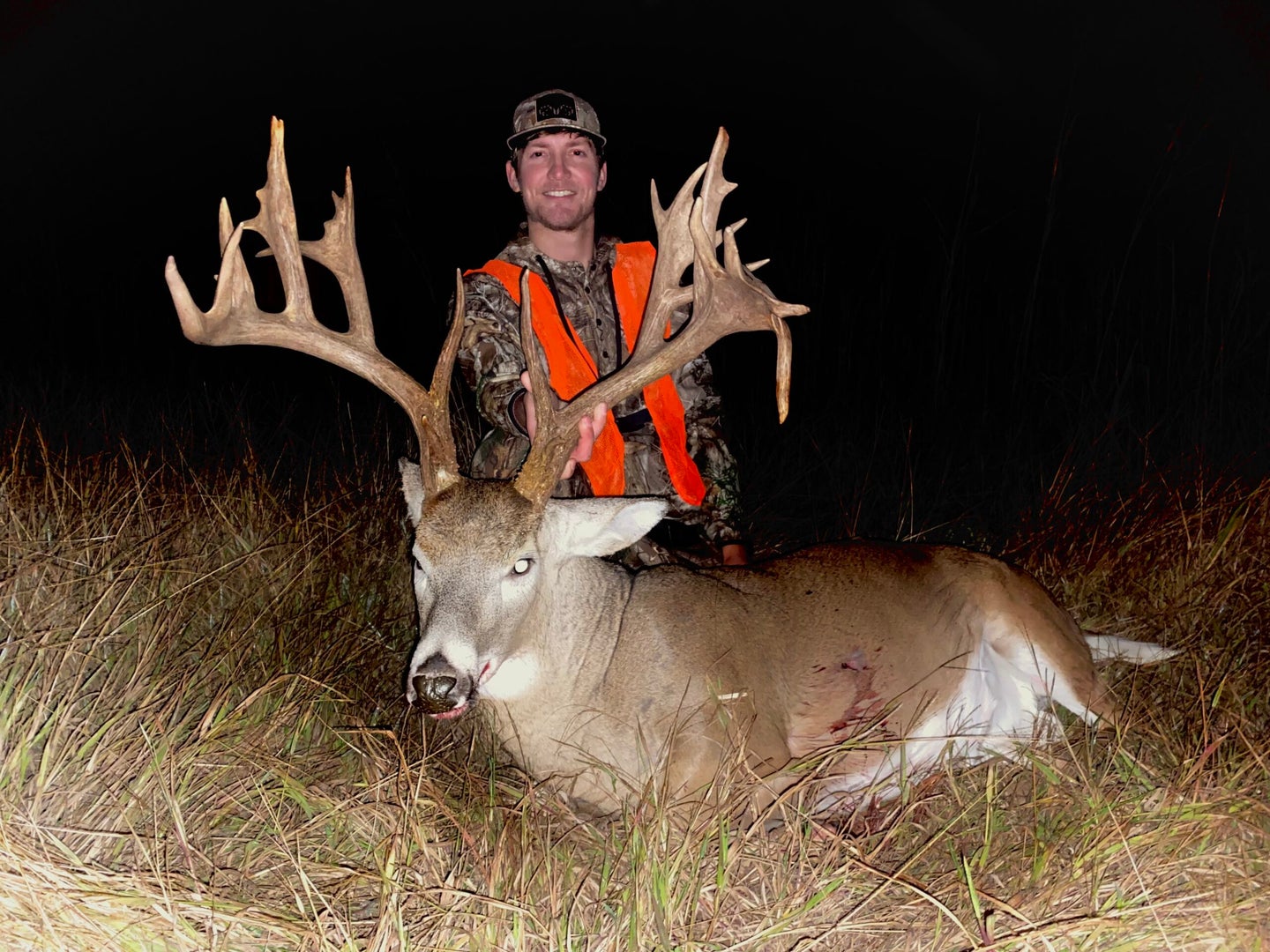 man in orange vest stands behind dead deer with incredibly large non-typical rack