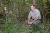 conservation officer crouches in the woods and smiles at camera