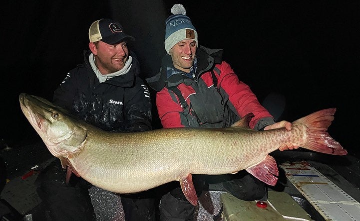 Two men pose with giant muskie at night