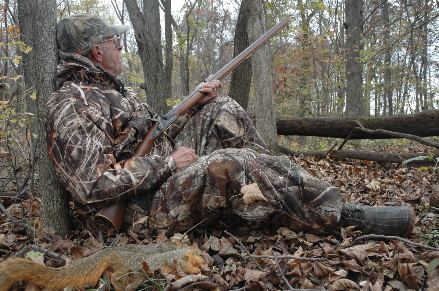 Hunter sitting against a tree with a black powder long rifle.