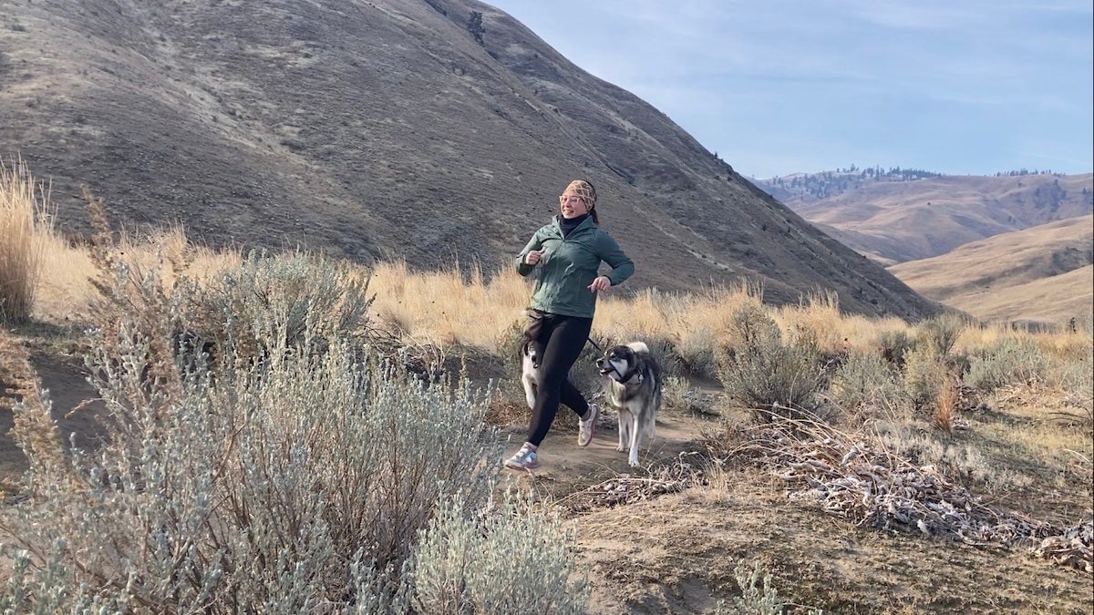 Female hiker wearing Jack Wolfskin Prelight Jacket while running with dogs