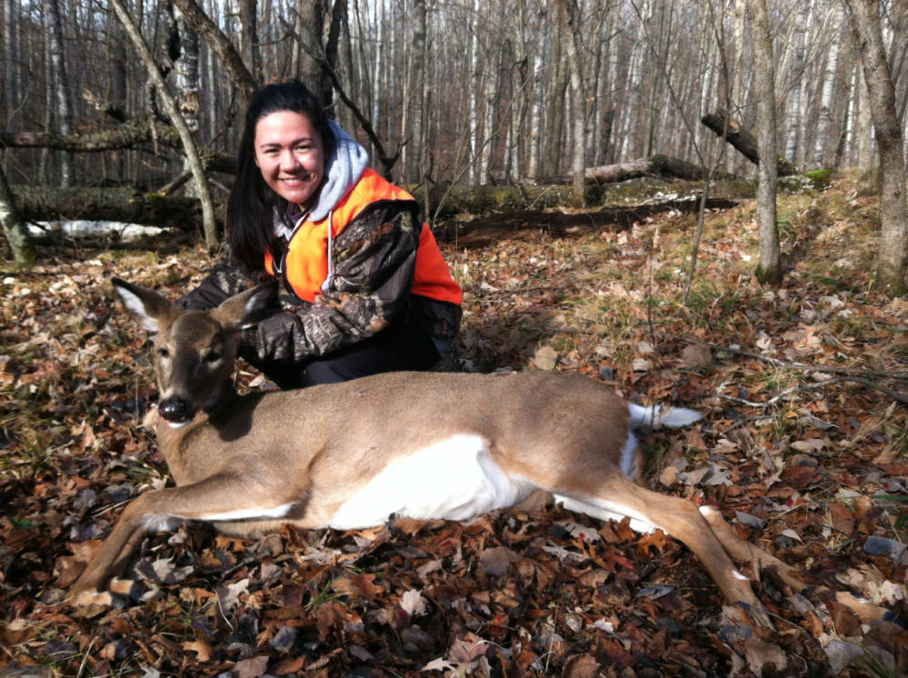 young female hunter kneels behind dead whitetail doe