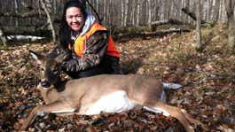 young female hunter kneels behind dead whitetail doe