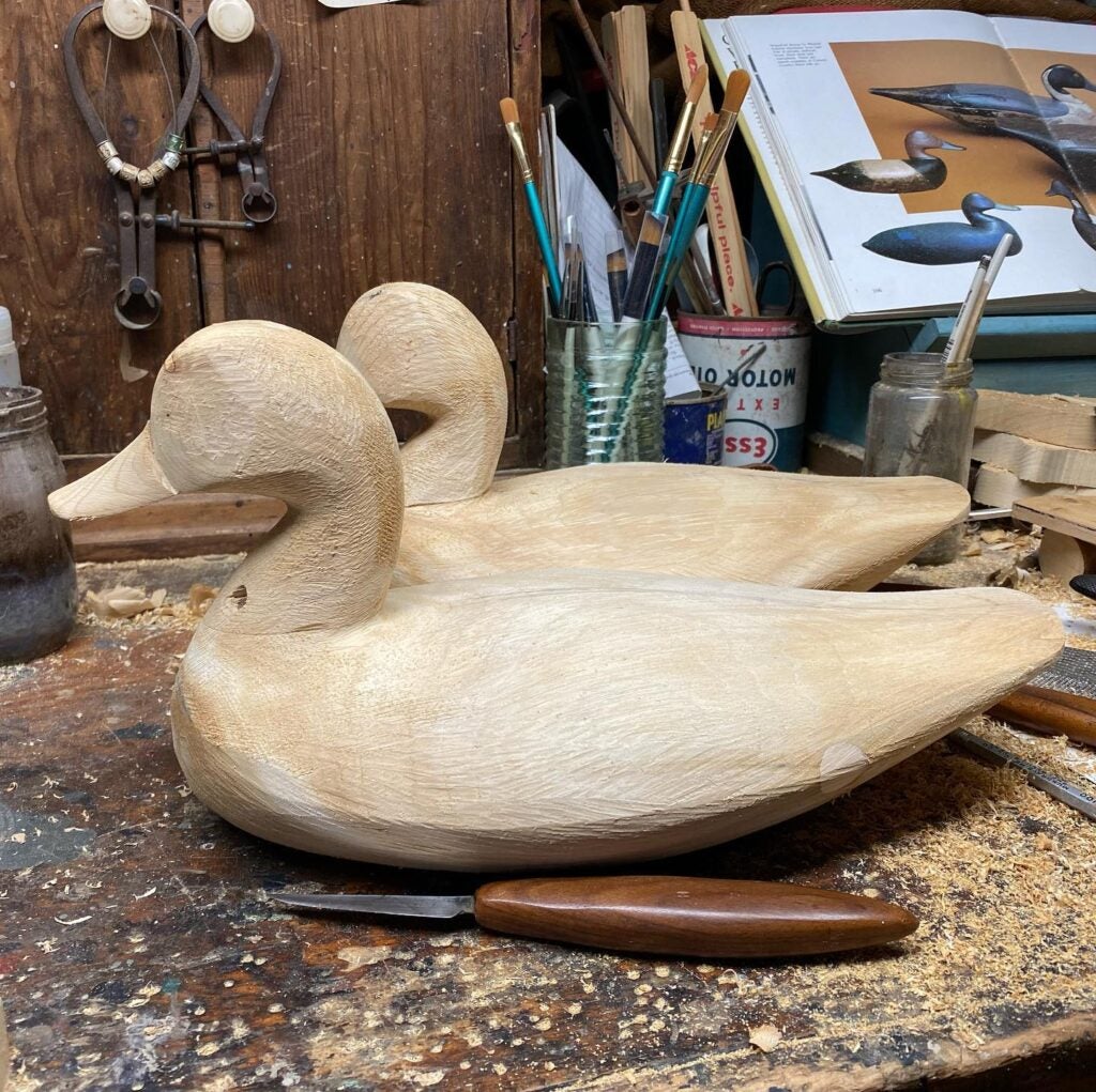 Hand-carved wooden decoys on a work bench without any paint.