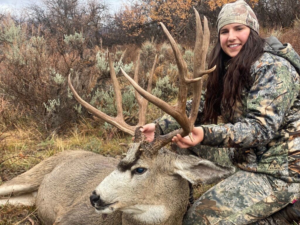 female hunter poses with dead deer